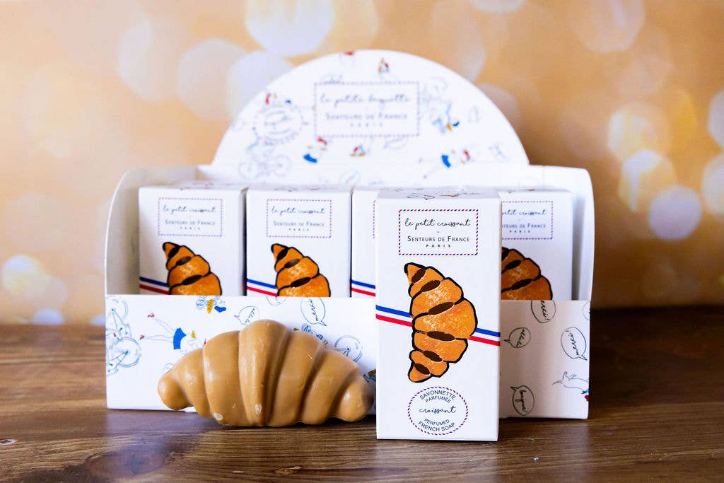 Packaging of croissant-shaped soap bars with decorative labels on a wooden surface.