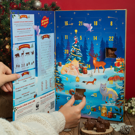 Person opening a Christmas advent calendar with festive design and small chocolate figurines.