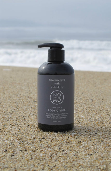 a bottle of Nomo Body cream on a beach