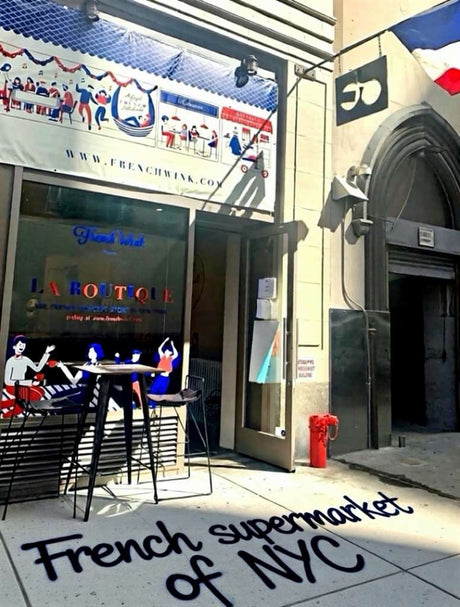 Entrance of a French supermarket in New York City with outdoor seating and “French supermarket of NYC” painted on the sidewalk