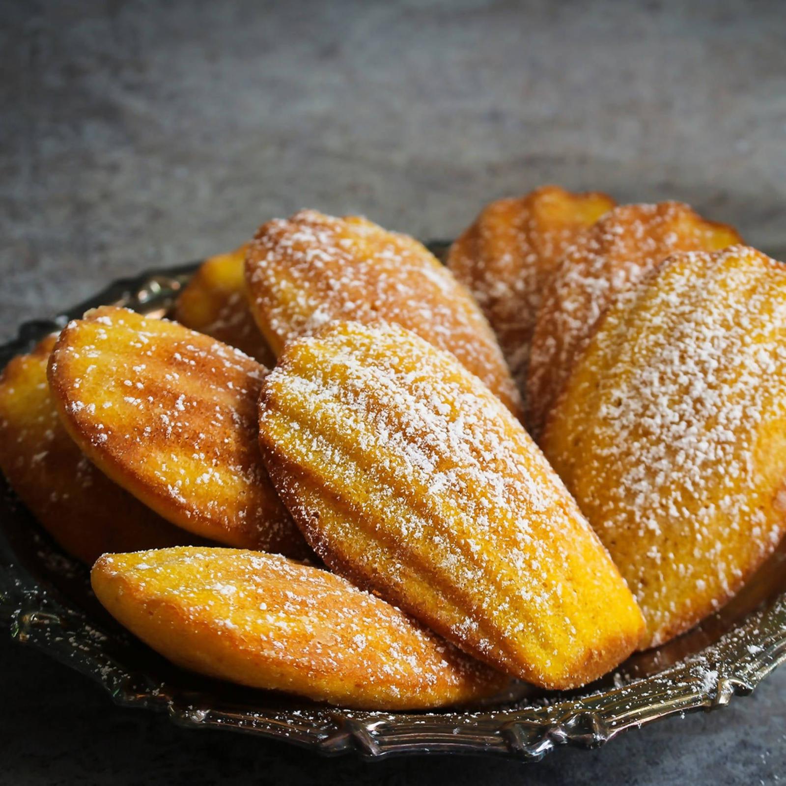 French madeleines dusted with powdered sugar and served on a dark plate