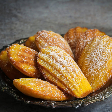 French madeleines dusted with powdered sugar and served on a dark plate