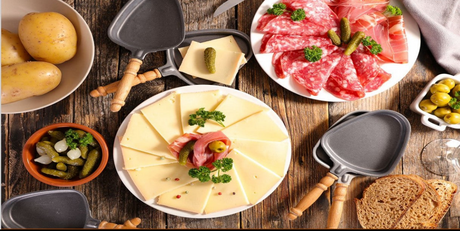 French raclette spread with sliced raclette cheese, charcuterie, potatoes, pickles, and mini raclette pans.