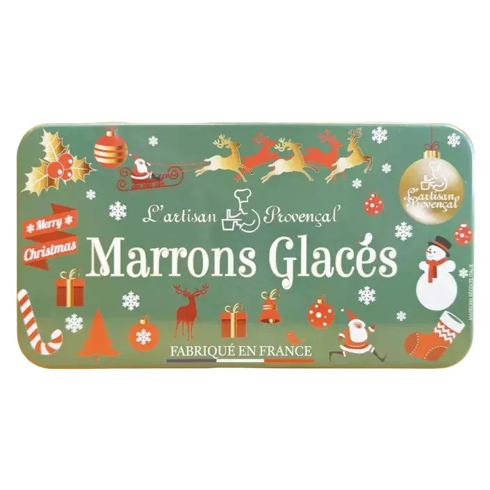 A rectangular metal tin of L'Artisan Provençal Marrons Glacés, decorated with a festive Christmas theme on a muted green background. The tin features illustrations of Santa Claus, reindeer, a snowman, gifts, and candy canes, with the brand name 'L'Artisan Provençal' and product name 'Marrons Glacés' printed in white.