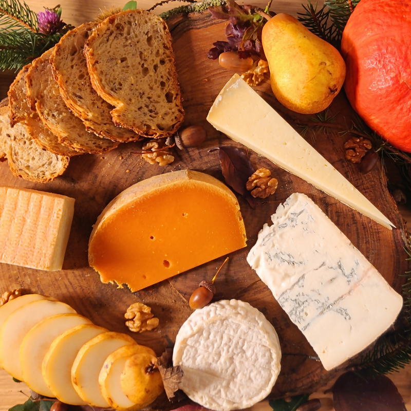 Assorted cheeses and bread on a wooden board with pears and nuts.