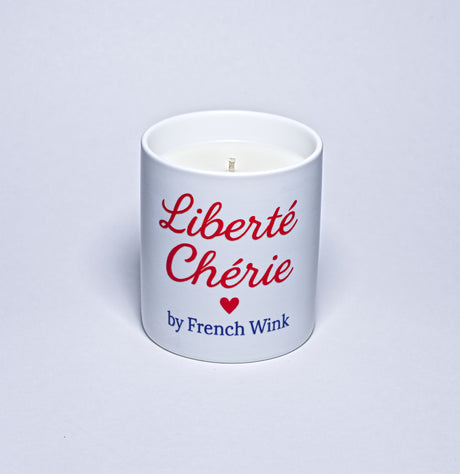White candle with red text 'Liberté Chérie' and a heart symbol, branded by French Wink on a light gray background.